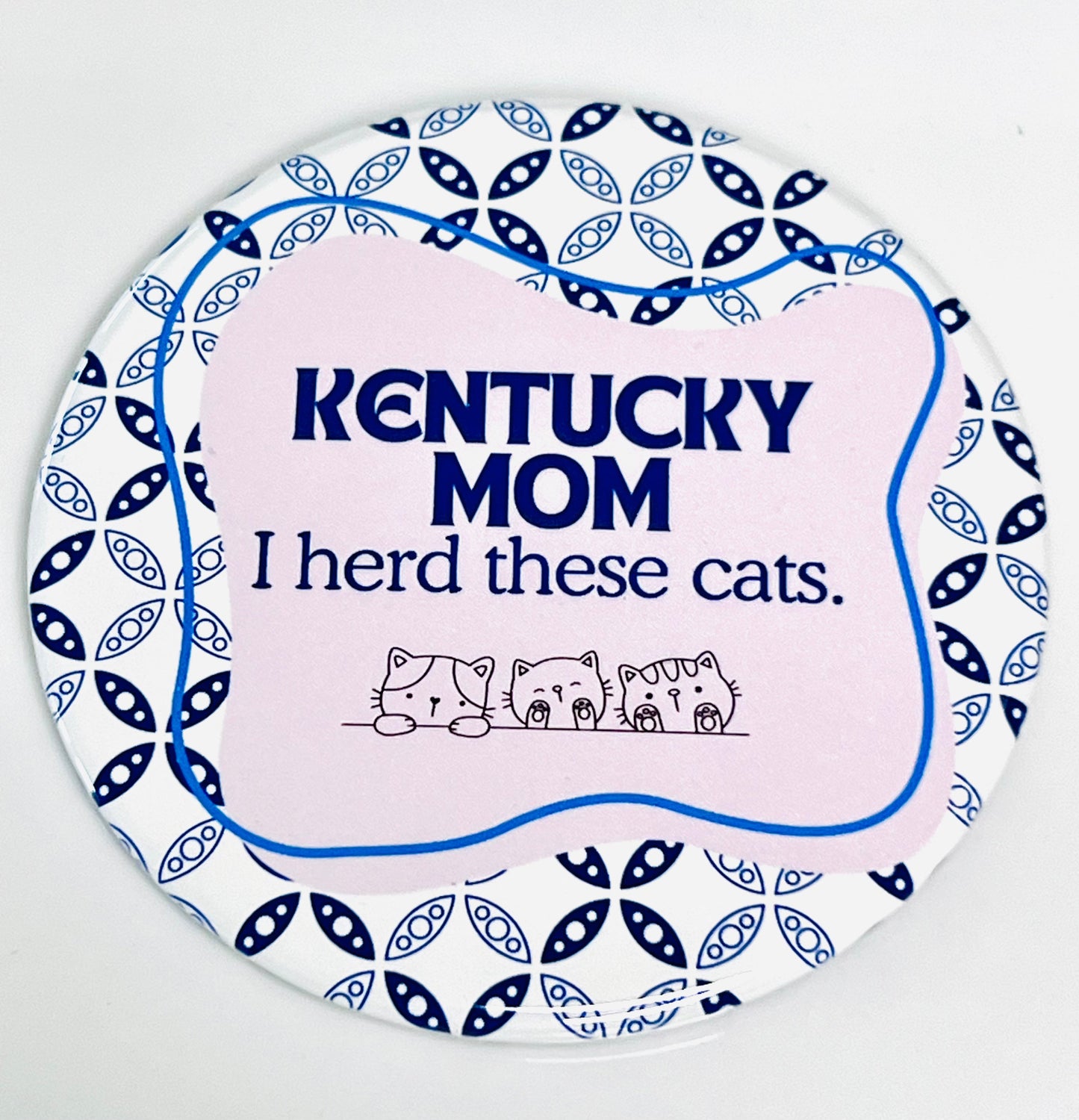 Round button with 'Kentucky Mom I herd these cats' text and cat illustrations on a pink and white, blue patterned background