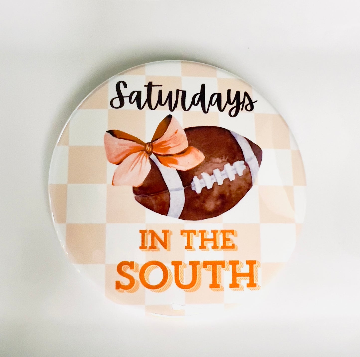 Round button with football, orange bow, and text 'Saturdays in the South' on an orange checkered background.