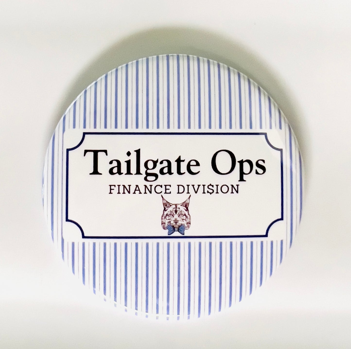 Round button with 'Tailgate Ops Finance Division' text and a wildcat illustration on a blue and white striped background