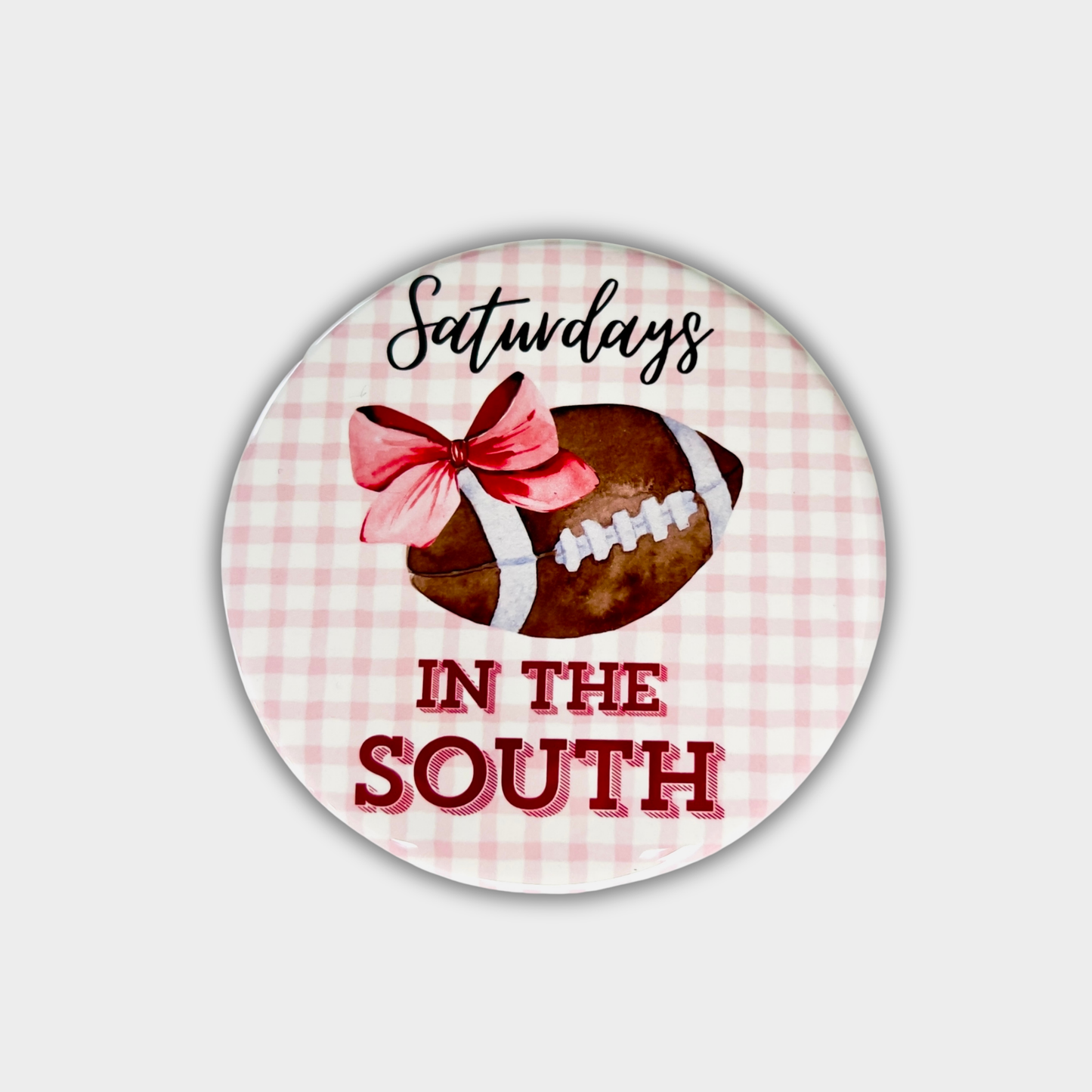 Round button with a football, bow, and text 'Saturdays in the South' on a pink checkered background.