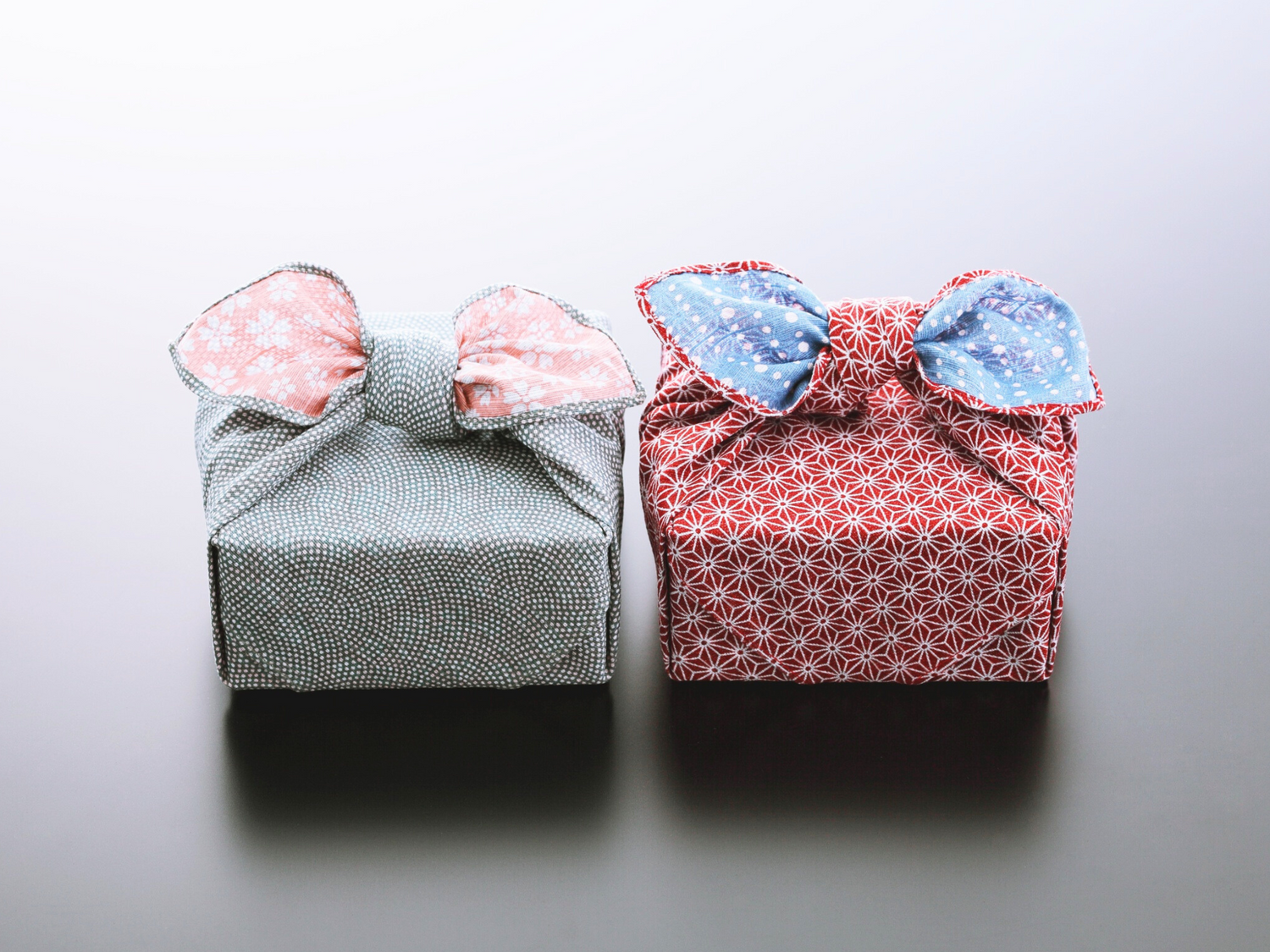 Two fabric wrapped packages with decorative bows on a light gray background