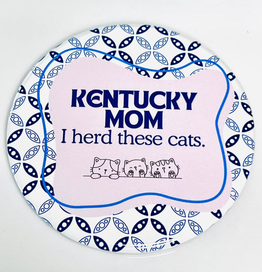 Round button with 'Kentucky Mom I herd these cats' text and cat illustrations on a pink and white, blue patterned background