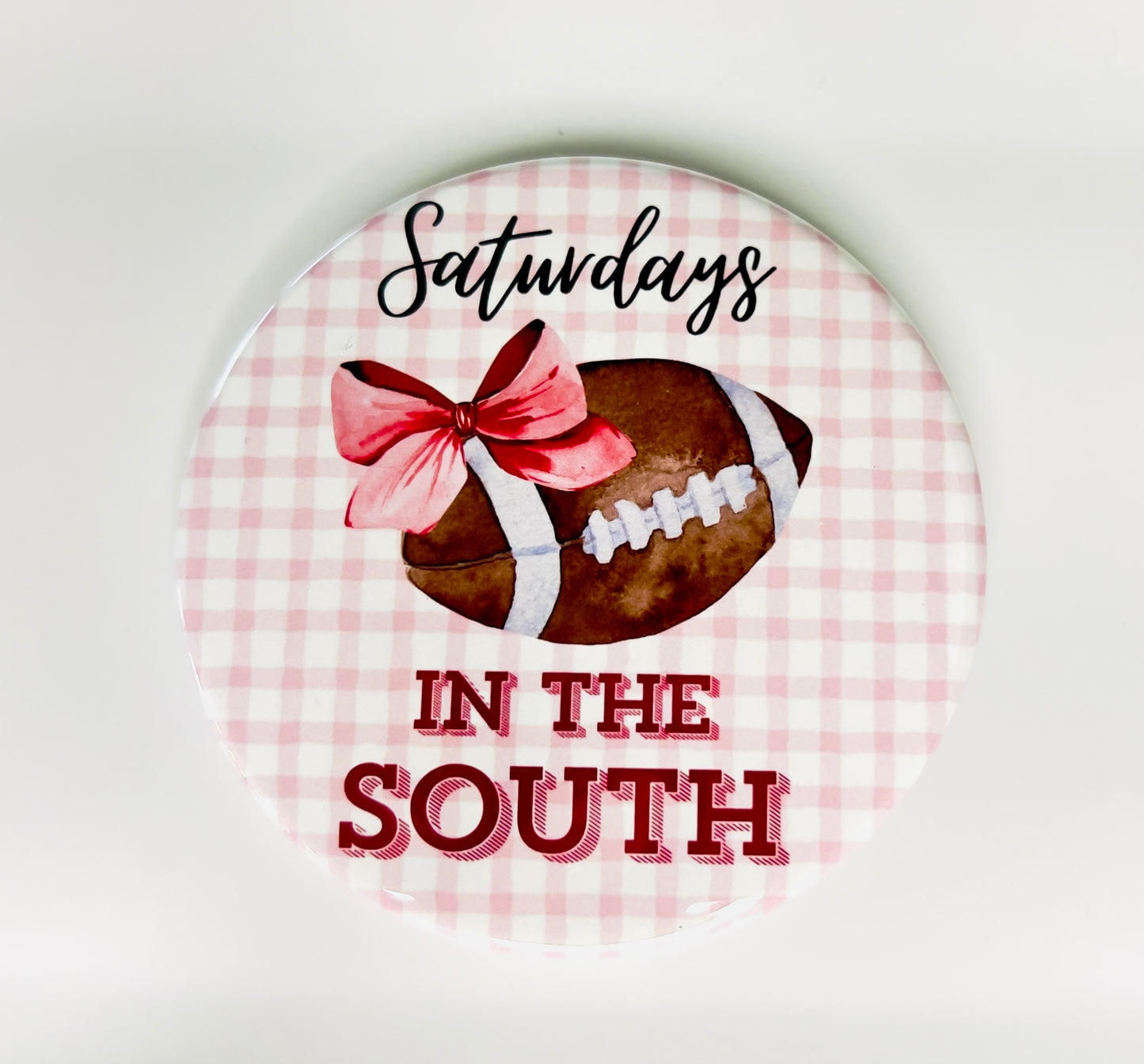 Round button with a football, bow, and text 'Saturdays in the South' on a pink checkered background.