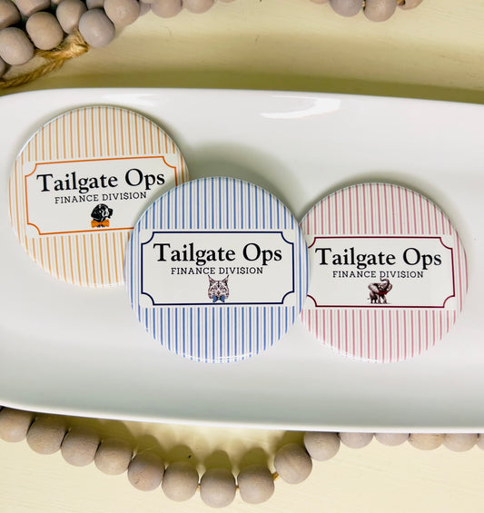 Three 'Tailgate Ops Finance Division' buttons in different colors with different mascots on a white tray