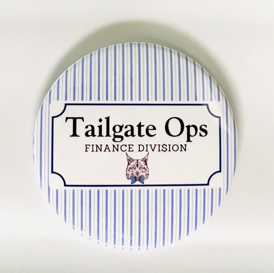 Round button with 'Tailgate Ops Finance Division' text and a wildcat illustration on a blue and white striped background