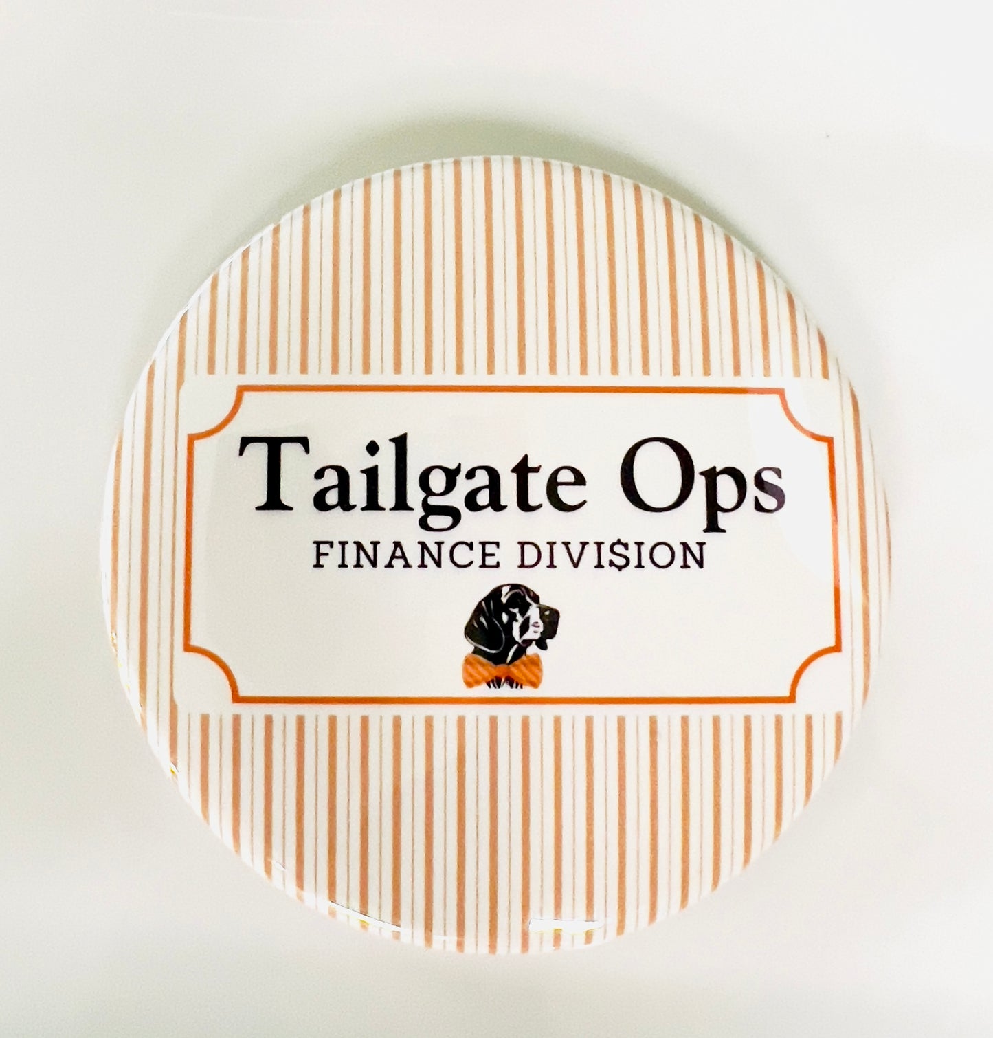 Round button with 'Tailgate Ops Finance Division' text and a dog illustration on an orange and white striped background