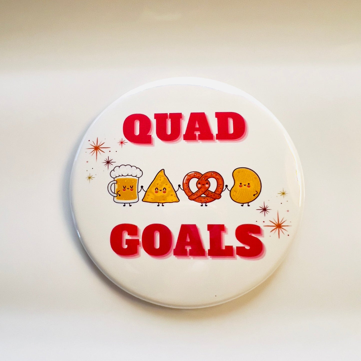 Button badge with 'Quad Goals' text and cartoon snack friends holding hands on a white background