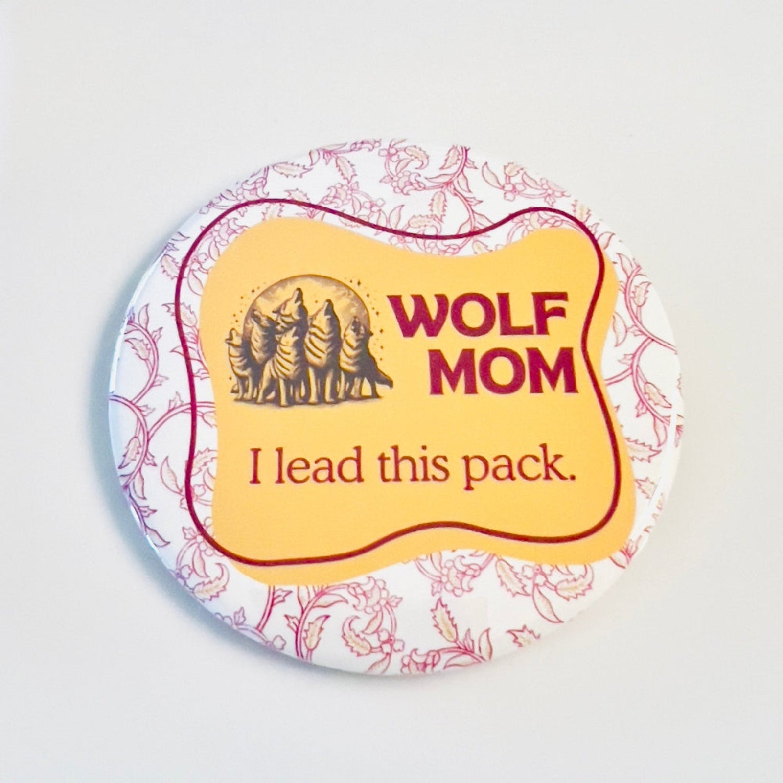 Button badge with 'Wolf Mom' text and wolf pack illustration on a decorative background